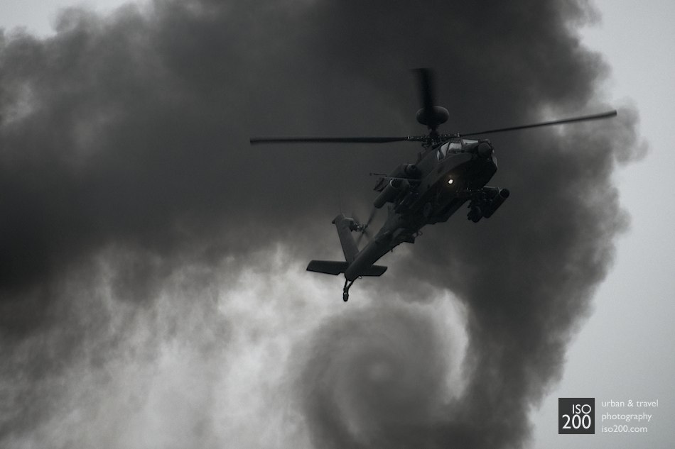 A British Army Air Corps Apache AH Mk 1 attack helicopter hovers in front of swirling black clouds of smoke.